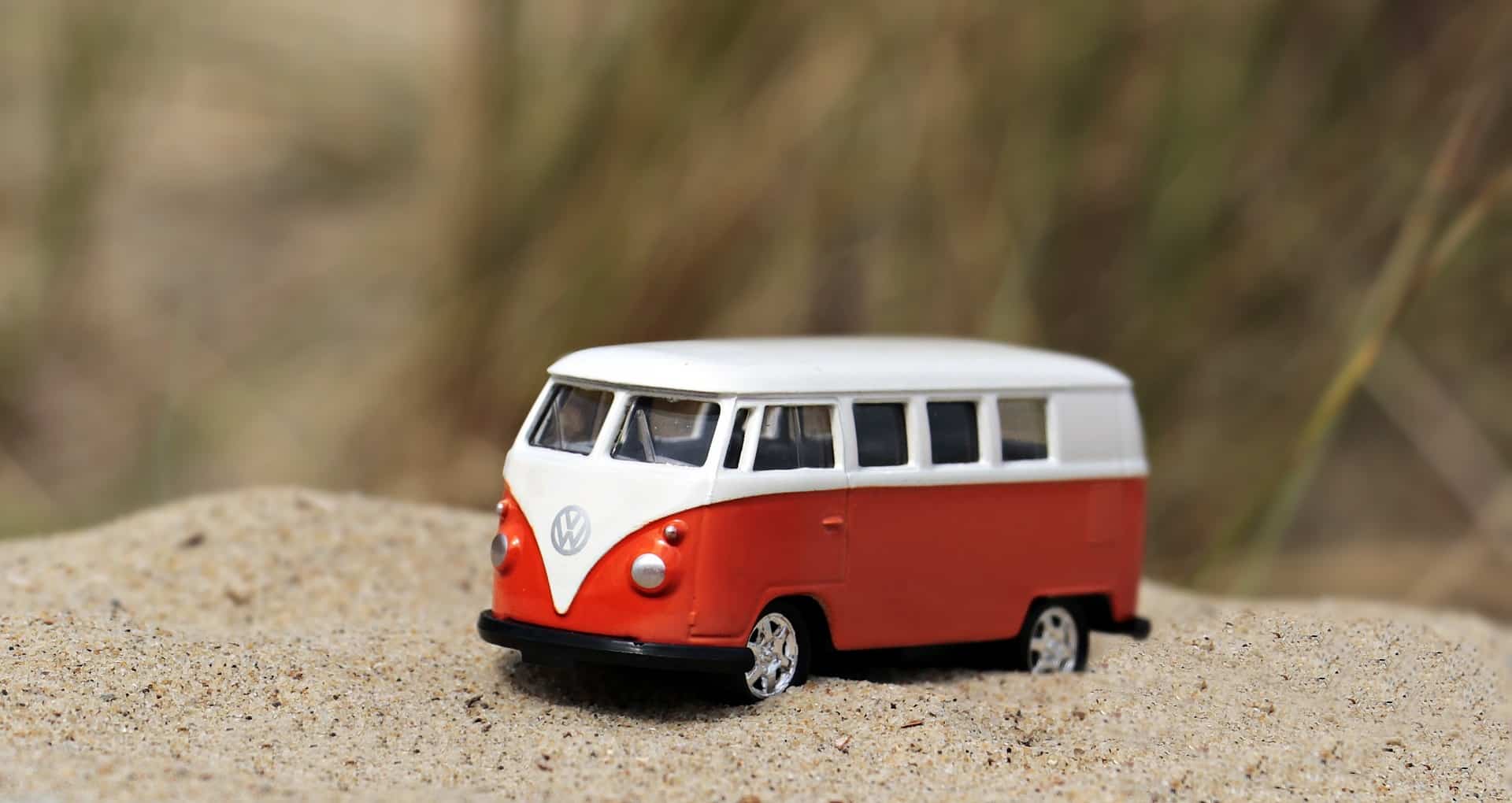 Un jouet représentant un autocar de la marque Wolswagen orange et blanc, est posé sur du sable.
