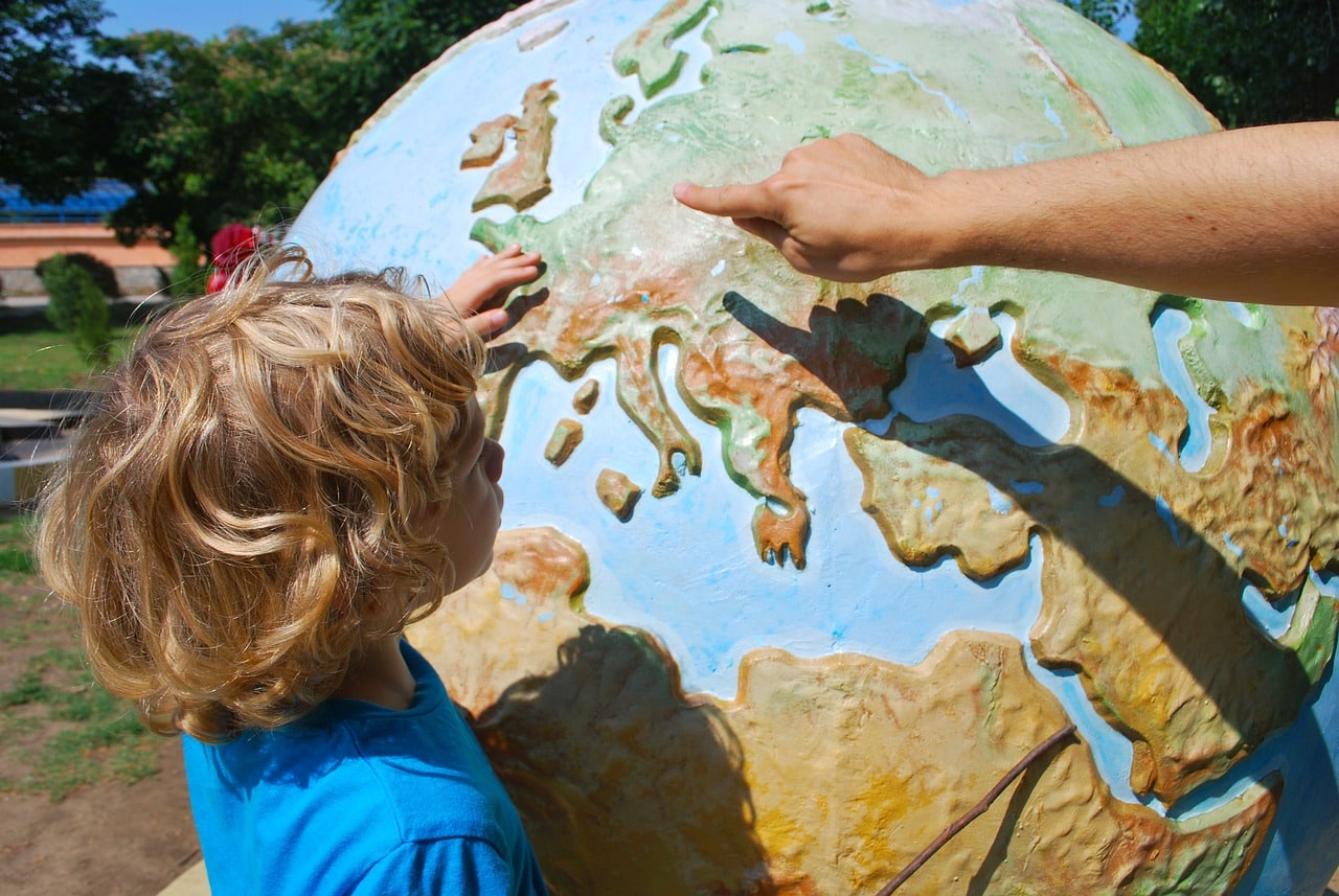 Enfant regardant un globe en volume. La main d'un adulte pointe l'europe du doigt.